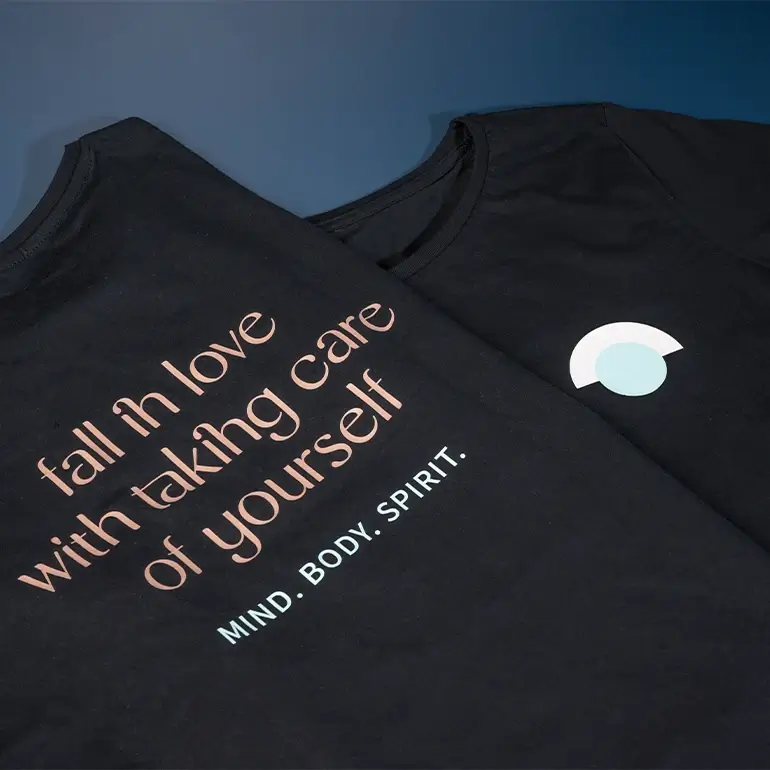 Nahaufnahme des mit dem Spruch "fall in love with taking care of yourself" bedruckten schwarzen Team-Shirts von Body & Soul